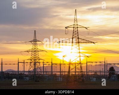 View of a high voltage electrical substation with transmission lines and transformers during dramatic sunset sky in a rural area. Stock Photo