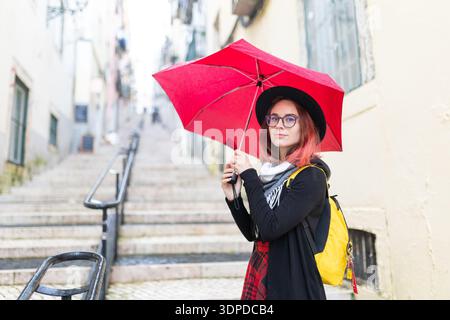 Young woman holding red umbrella exploring city steps Stock Photo
