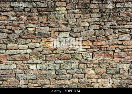 Irregular stone wall with natural limestone bricks in various shades of beige and brown. The roughly cut stones are unevenly stacked, showcasing a rus Stock Photo
