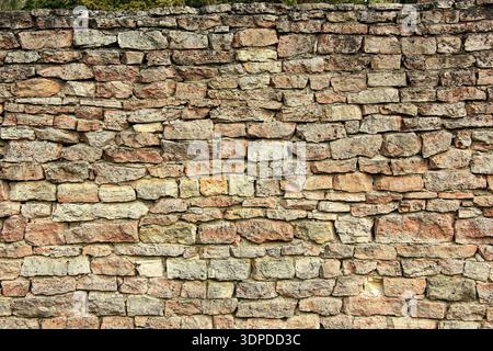 Irregular stone wall with natural limestone bricks in various shades of beige and brown. The roughly cut stones are unevenly stacked, showcasing a rus Stock Photo