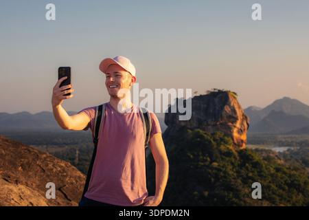 Tourist with backpack taking selfie on Pidurangala Rock with Sigiriya Rock in background. Travel adventure and exploration in Sri Lanka. Stock Photo