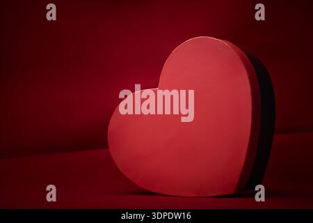 empty red heart-shaped cardboard box on red background, smooth matte finish gift container, valentine's day mockup, romantic gift packaging or luxury Stock Photo