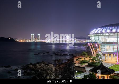 A serene nighttime long exposure of the illuminated Nurimaru APEC House on Dongbaekseom Island, featuring the Gwangan Bridge and the Busan city Stock Photo