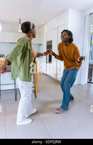 African American couple holding hands and dancing in modern kitchen near island in casual attire Stock Photo
