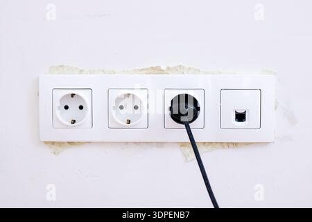 White wall outlet with black plug mounted on stained plaster, triple socket strip including network port, black cable Stock Photo
