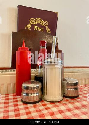 the condiments and menu with tomato ketchup and brown sauce plastic bottles, glass sugar dispenser ,vinegar bottle and salt and pepper sellars Stock Photo