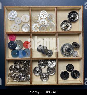 Vintage wooden tray with assorted old buttons in compartments. Varieties from past generations, showing age patina and craft history. Stock Photo