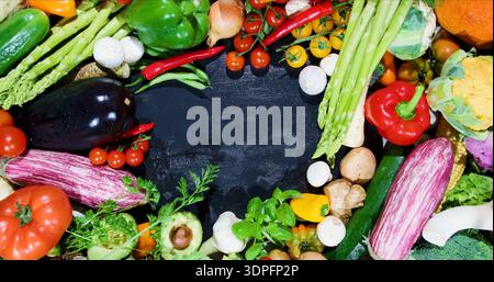 Fresh vegetables arranged on a dark surface for a cooking display with various colors and shapes present in the arrangement Stock Photo