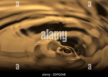 285.An abstract, close-up photograph of golden-hued liquid ripples expanding in a dynamic circular pattern. The surface shows light reflections and sh Stock Photo
