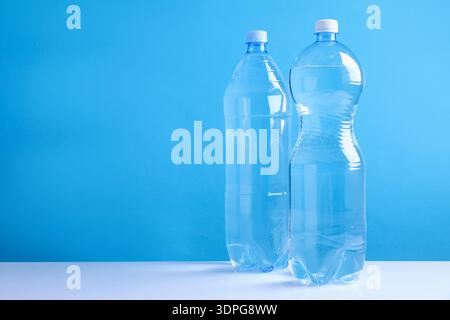 Bottles of fresh water on white table against light blue background, space for text Stock Photo
