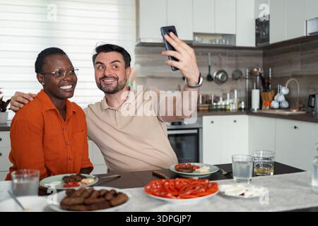 Happy multi-ethnic couple taking a selfie while having lunch in the kitchen Stock Photo