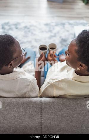 Two black women sitting on sofa drinking coffee at home Stock Photo