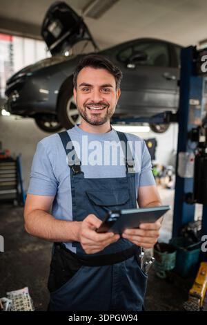 Car mechanic using a digital tablet and smiling at the camera in Stock Photo