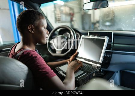 Young female mechanic running diagnostics on a car with a laptop Stock Photo
