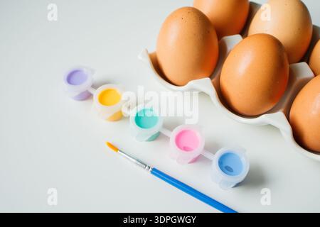 Easter eggs on a stand with paints and brush on white background close up. Eggs decoration before Easter holidays. Stock Photo