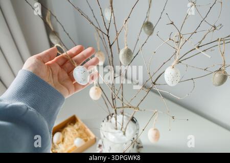 House decorating before Easter holidays: hanging small souvenir eggs on handmade Easter tree at home close up Stock Photo