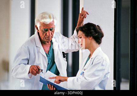 Two doctors engage in conversation while reviewing a patient file in a hospital setting. They focus on the details in the document, highlighting their Stock Photo