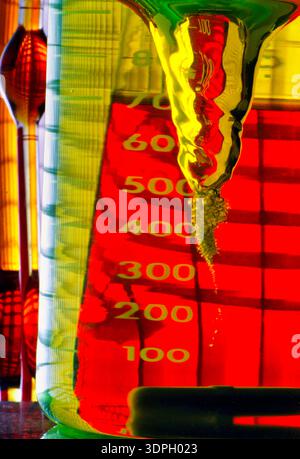 A laboratory beaker shows colorful liquids mixing and creating bubbles. The scale on the beaker displays measurements. Light plays through the liquids Stock Photo