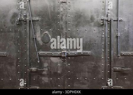 A heavy metal door is secured with bolts and rivets. The surface shows signs of wear. This door is in an industrial area, reflecting a past use in man Stock Photo