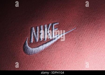Embroidered Nike logo with swoosh on salmon pink fabric. Close-up detail of silver thread branding on high-quality cotton sweatshirt material. Stock Photo
