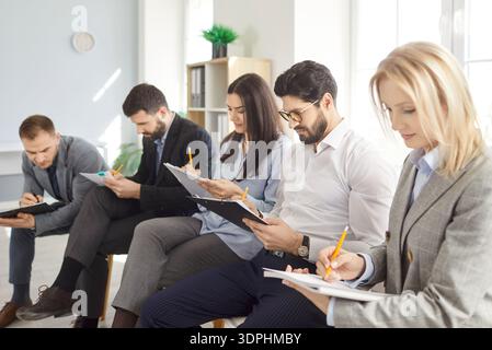 Business people sitting in a row working during a meeting or job conference making notes in notepad Stock Photo