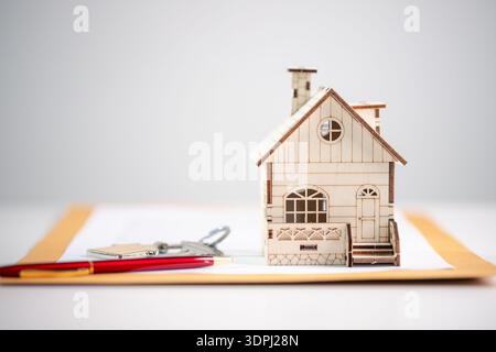 Miniature wooden house on document envelope with pen and house keys on white background, representing real estate paperwork, mortgage approval, home b Stock Photo