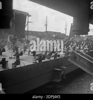 An impressive archival photograph from the 1960s depicting Soviet welders at work on a massive steel grid structure during the construction of the Slavyanskaya Thermal Power Plant (GRES) in Nikolaevka, Donetsk region. The scene captures the intense manual labor and technical skill required to assemble the industrial foundation of the energy giant. Sparks fly as workers in protective masks meticulously weld components together against a backdrop of rising infrastructure. This authentic black and white image represents the creative spirit and the immense engineering scale of the peaceful Donbas Stock Photo