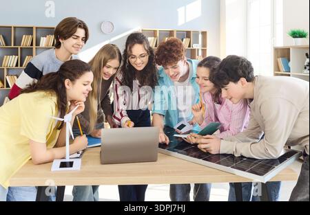 Students and teacher gathered at laptop with solar panel in modern classroom Stock Photo