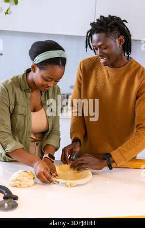 African American couple shaping pie dough in pan at kitchen counter in olive shirt brown sweater Stock Photo