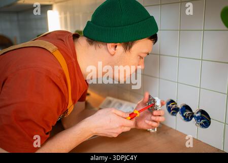 Professional electrician performing electrical installation work, connecting wires to a new power socket on a tiled kitchen wall during a home improvement project or renovation Stock Photo