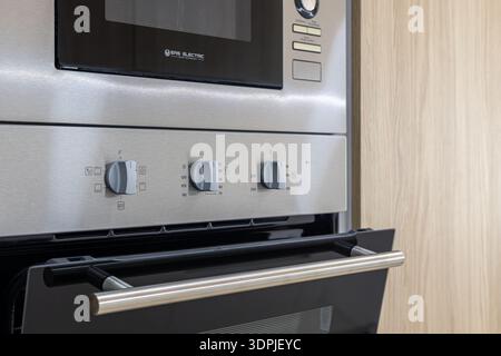 Close up of modern stainless steel built in oven with control knobs and handle in contemporary kitchen interior. Stock Photo