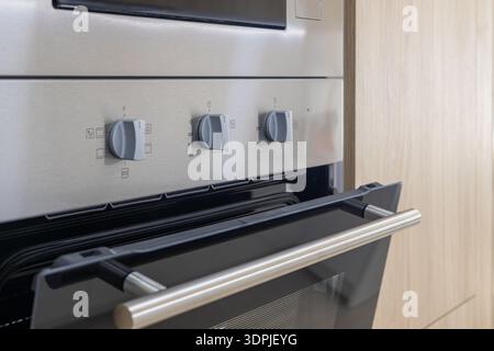 Close up view of stainless steel built in oven with control knobs and handle in contemporary kitchen cabinetry. Stock Photo