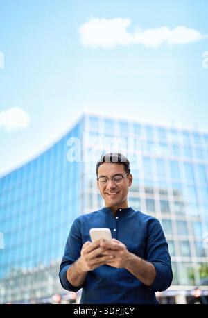 Happy Hispanic business man using mobile cell phone standing in city. Vertical Stock Photo