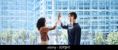 Two happy diverse young team business people give high five standing in office. Stock Photo
