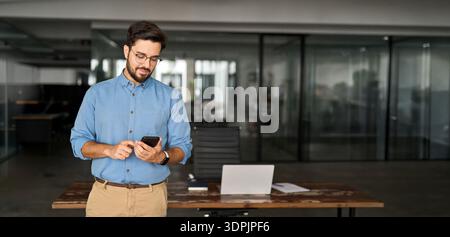 Smiling busy professional latin business man standing in office holding mobile cellphone.  Stock Photo