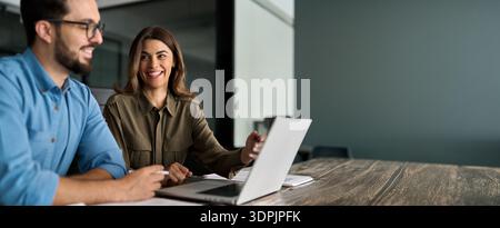 Happy female manager talking to male employee working on computer in office. Stock Photo