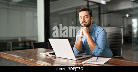 Young business man sitting at work desk in office with laptop, portrait. Stock Photo