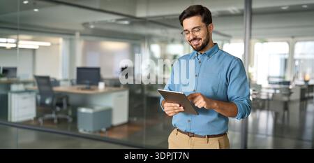 Smiling busy young business man manager using tablet standing in office. Stock Photo