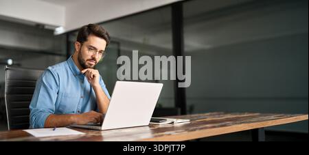 Busy latin business man thinking on online investment working on laptop. Stock Photo