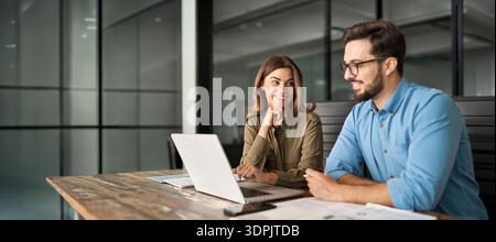 Two happy professional colleagues talking at meeting using laptop computer. Stock Photo