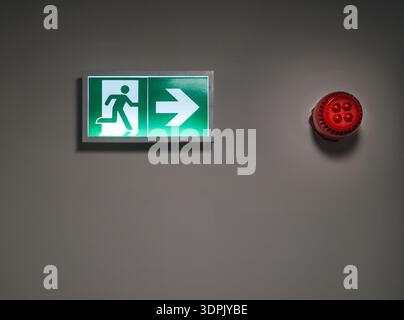 Emergency exit sign alarm siren office interior. Green evacuation symbol directional arrow safety equipment red warning device wall mounted workplace Stock Photo