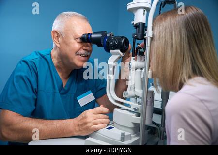 Smiling ophthalmologist testing eyesight of woman with special ophthalmological equipment Stock Photo