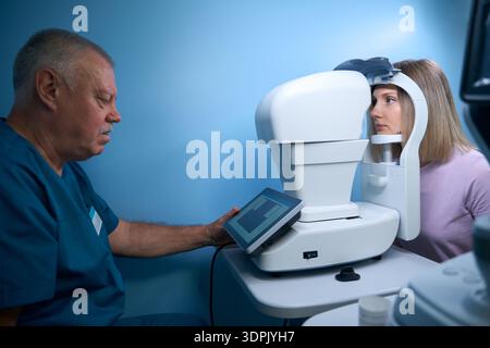 Male doctor ophthalmologist checking the eye vision of young woman in modern clinic Stock Photo