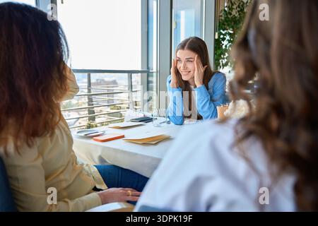 Smiling woman holding hands near face while talking with her friends in restaurant Stock Photo
