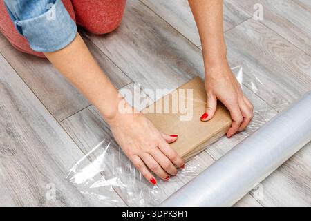 A woman wraps a parcel in plastic wrap.  Stock Photo