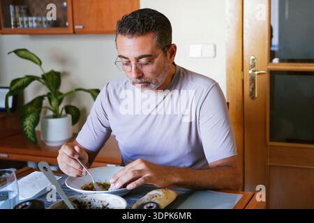 Serene midday meal scene featuring man focused on eating in cozy kitchen environment Stock Photo