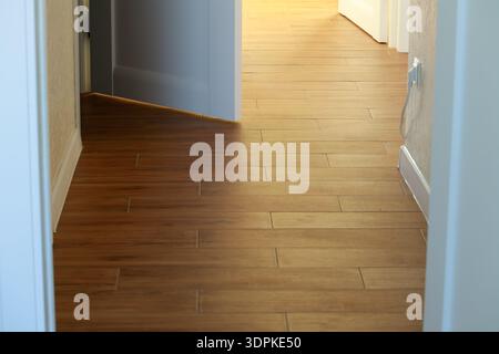 A bright hallway with wooden plank flooring illuminated by natural sunlight, leading towards an open doorway and an electrical outlet on the wall Stock Photo