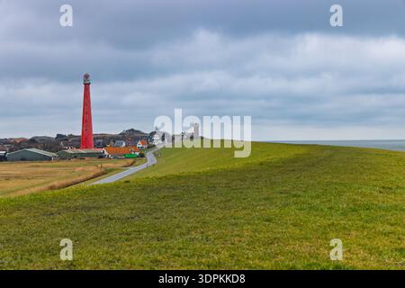 The iconic red lighthouse Lange Jaap in Huisduinen, Den Helder, standing tall behind the sea dike under a dramatic sky. Tallest cast-iron tower. Stock Photo
