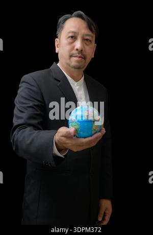 professional man in a black suit holding a small globe against a dark background, symbolizing global responsibility, sustainability, environmental awa Stock Photo