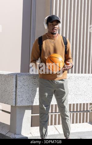 African American man holding orange basketball standing behind speckled concrete barrier on terrace Stock Photo